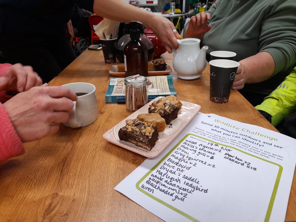 Close up of hands drinking coffee and cake and a task list of conservation activities